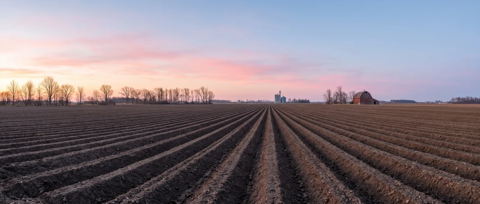 Generated scene: a freshly ploughed field at sunrise, straight brown furrows running to a flat horizon with bare trees, a grain silo and a red barn.